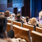 Speaker giving a talk in conference hall at business event. Rear view of unrecognizable people in audience at the conference hall. Business and entrepreneurship concept